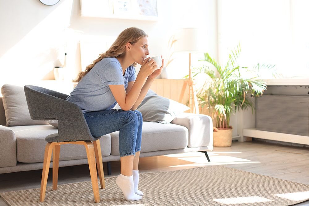 Woman sitting in chair drinking coffee in apartment living room