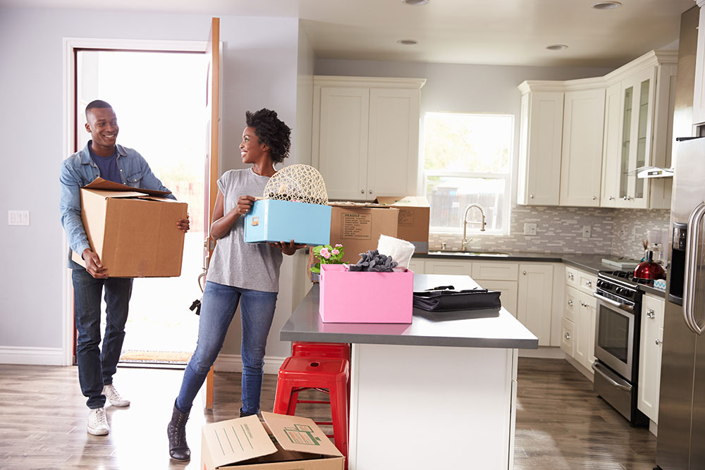 Couple moving into new apartment in kitchen holding boxes