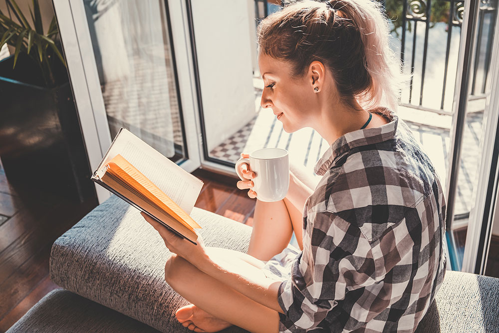 Woman sitting on balcony drinking coffee and reading a book