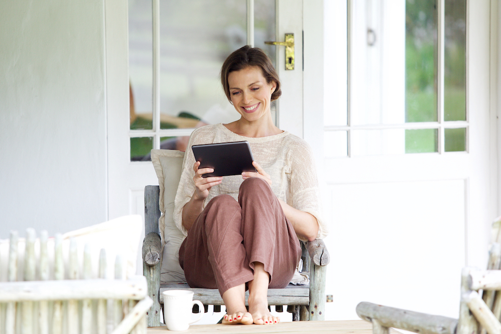 A happy woman reading on her tablet while sitting on her apartment balcony 