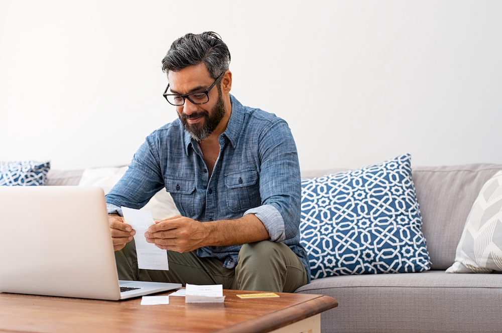 A smiling man paying bills using his laptop computer