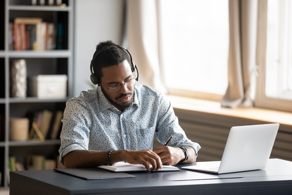 A young man wearing headphones while working from home at the table