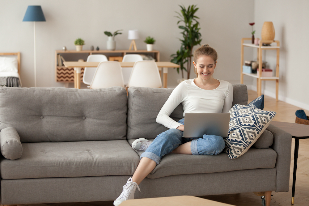 A smiling young woman sitting on her sofa working at one of the best studio apartments for rent in Kansas City